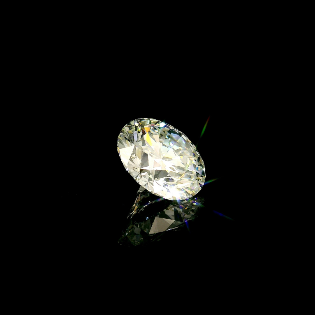 A 3 ct. Round Cut Lab Grown Diamond sits on a reflective surface against a black background, showing flashes of light.