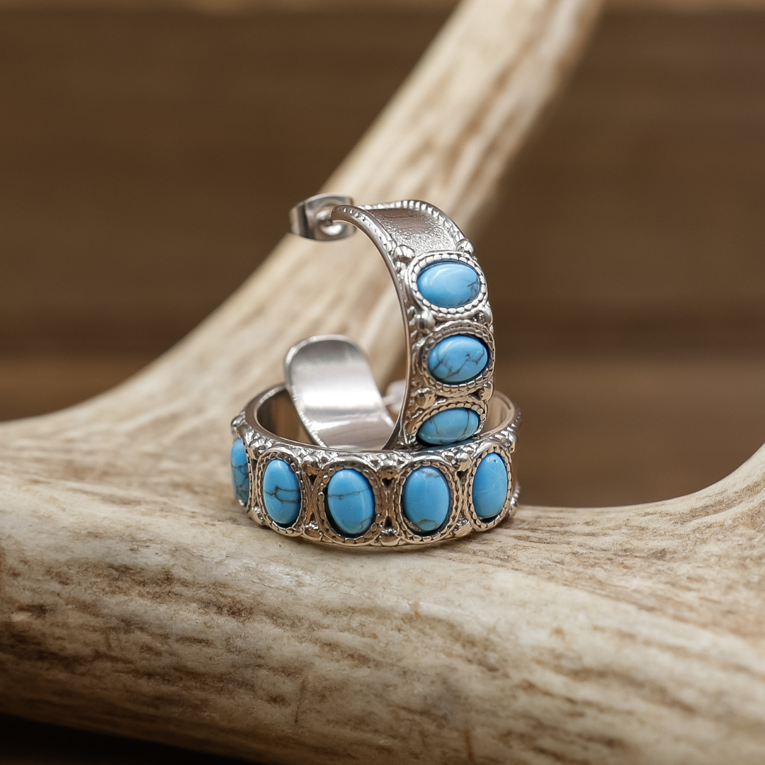 Hoop earrings with oval turquoise stones, displayed on a natural antler against a warm brown background.