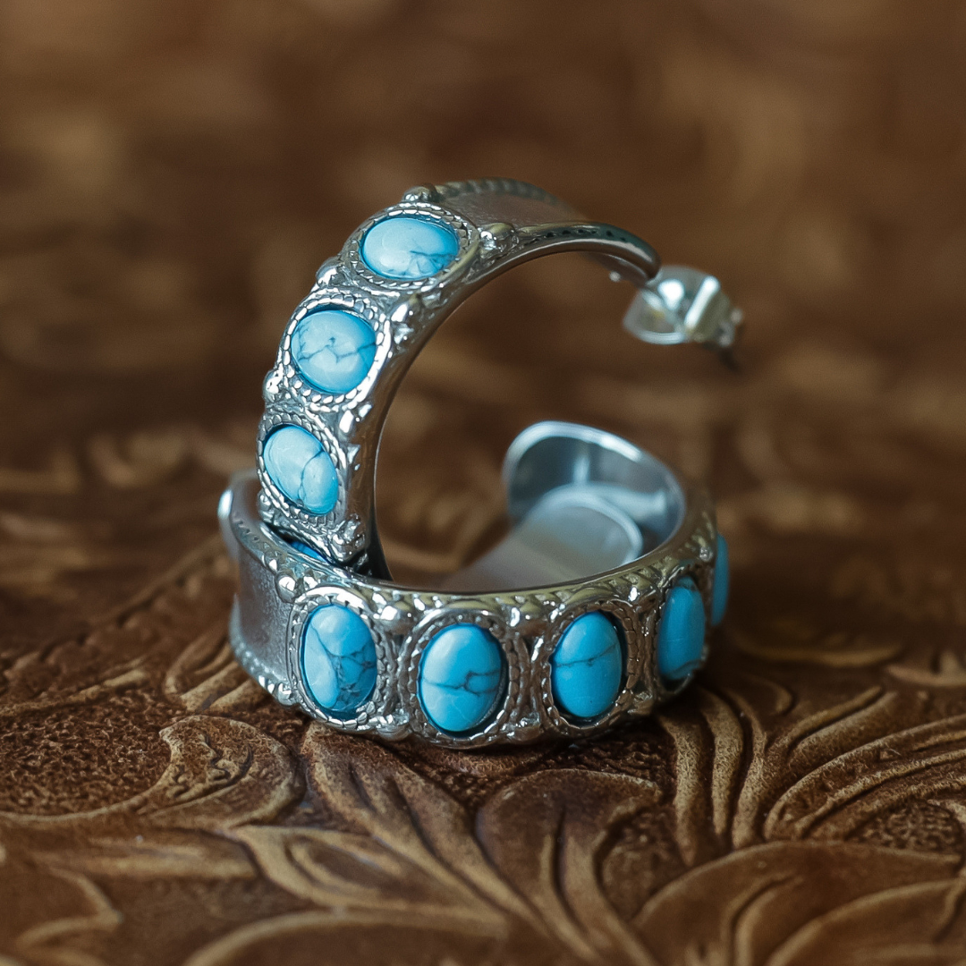 Silver-toned hoop earrings embellished with multiple oval turquoise stones, displayed on a textured brown leather surface.