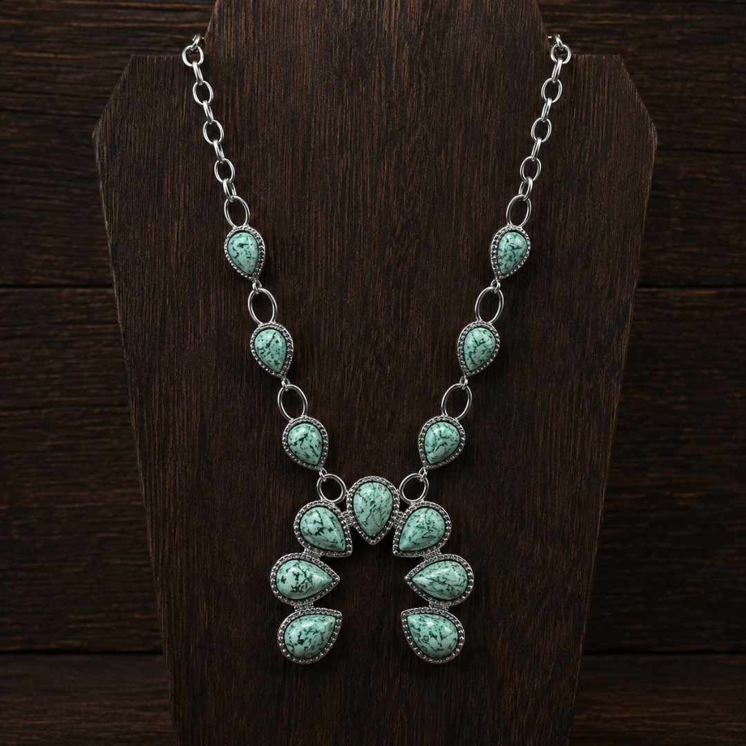 The Cornelia, a silver Western necklace featuring turquoise stones in teardrop settings, is displayed on a dark wooden stand.