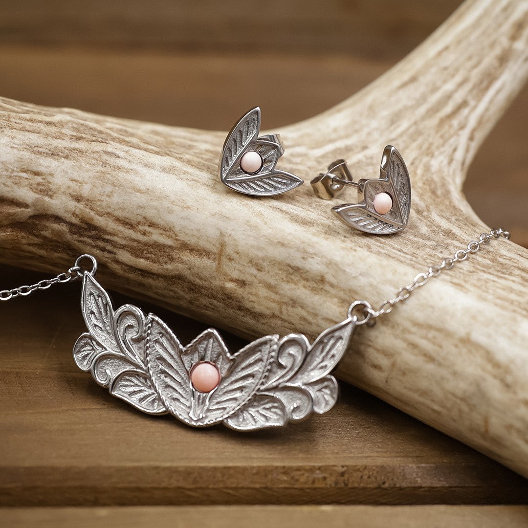 Silver necklace and earrings with intricate leaf designs and pink gemstones, displayed on a wooden surface with a piece of antler in the background. This elegant set pairs beautifully with The Dessie Stud Earrings for a unique, nature-inspired style.