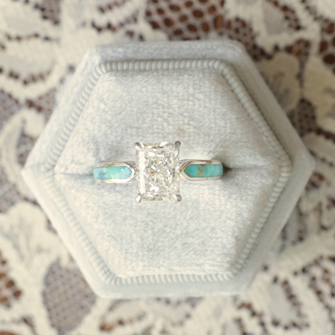 Introducing the Diamond Rochelle: a Western-inspired engagement ring showcasing a rectangular lab-grown diamond and turquoise inlay on a sleek silver band, presented in a light gray hexagonal velvet ring box and elegantly displayed atop delicate lace fabric.