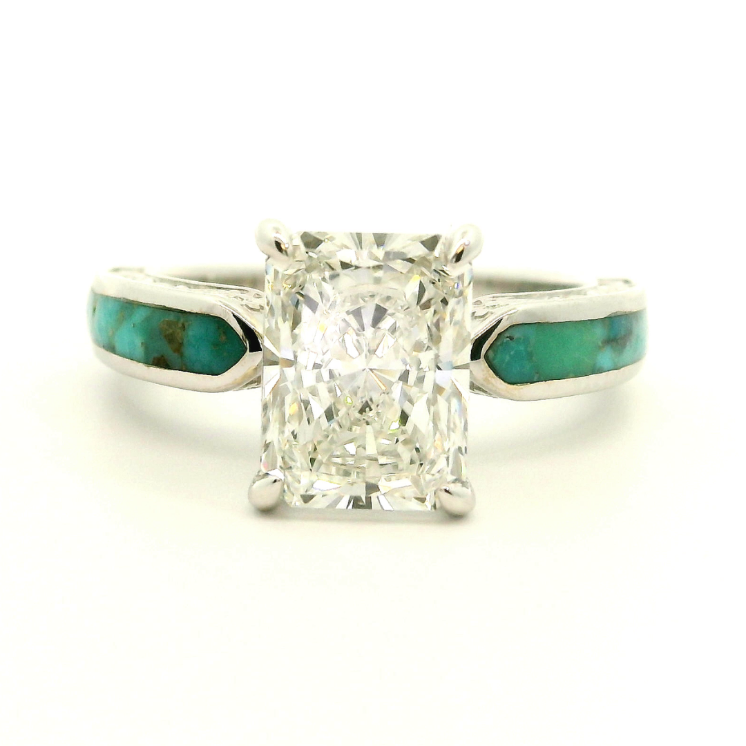 The Diamond Rochelle is a silver Western engagement ring showcasing a radiant-cut lab-grown diamond center stone with striking turquoise inlays on both sides of the band, displayed against a white background.
