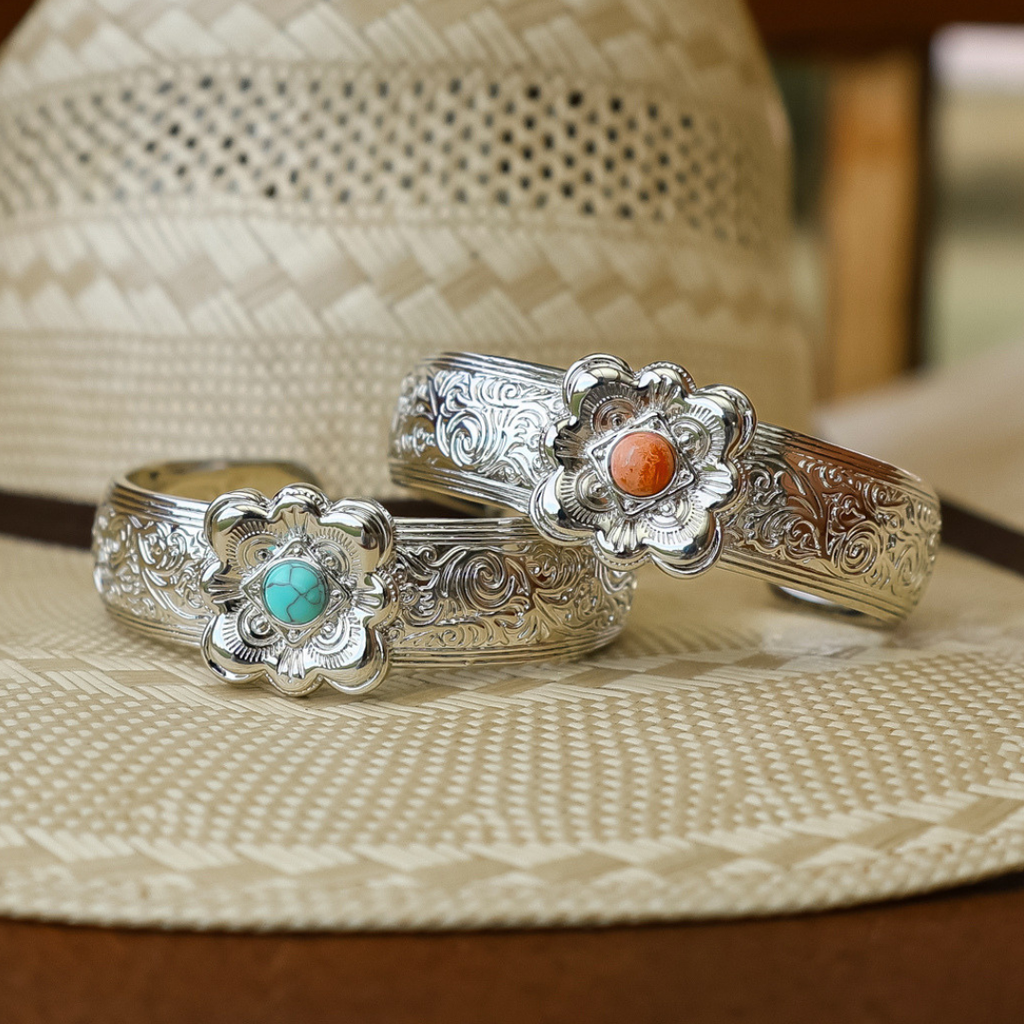 Certainly! Here’s the revised sentence using your product data: The Eloise Cuff, an ornate silver bracelet with a floral design and a striking turquoise centerpiece, makes for stunning statement jewelry when beautifully displayed atop a woven straw hat.
