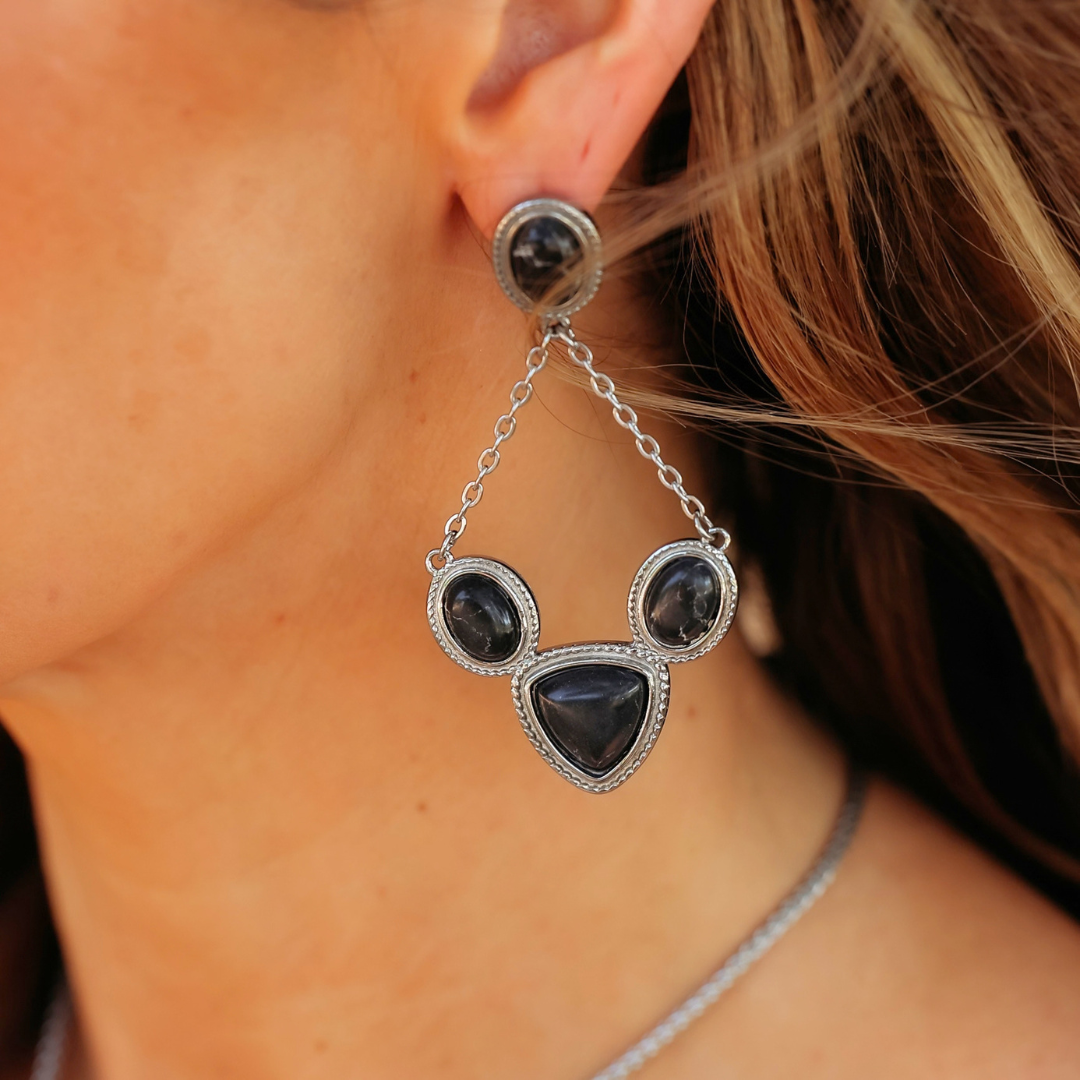 The Eve Drop Earrings are silver drop earrings featuring four black stones arranged in a triangular chain pattern, styled as Western jewelry.