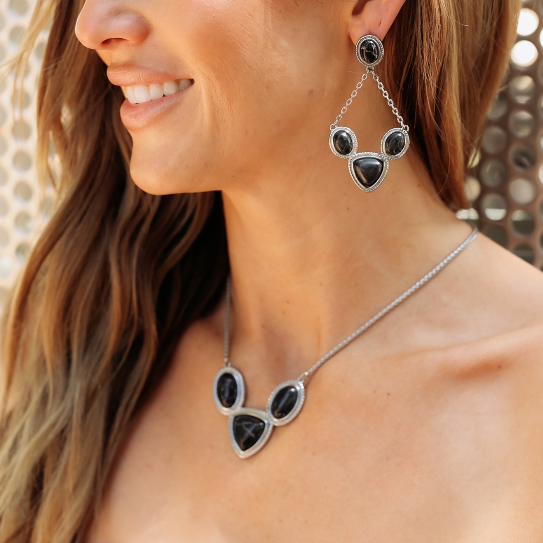 A woman wearing The Eve Drop Earrings and a matching necklace, both featuring triangular black stones set in silver Western-style frames.