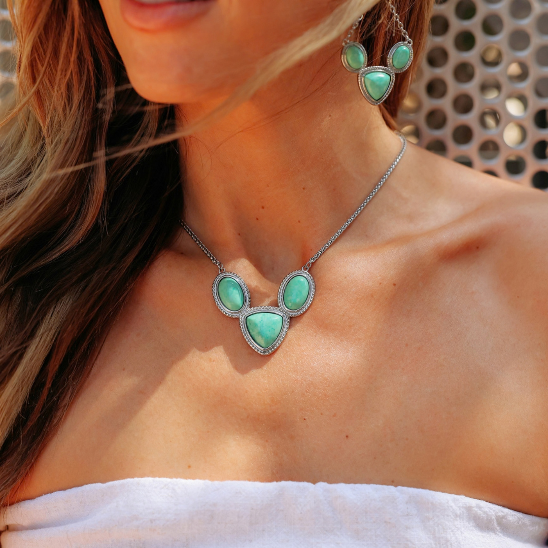 The Eve is a silver Western necklace and matching earring set featuring clusters of three green turquoise-colored teardrop stones with rope detailing.