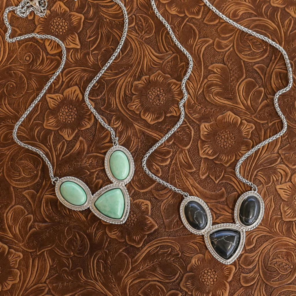 The Eve necklaces: two silver-tone pieces with rope detailing, one featuring light green oval and triangular stones, the other accented with dark gray stones.