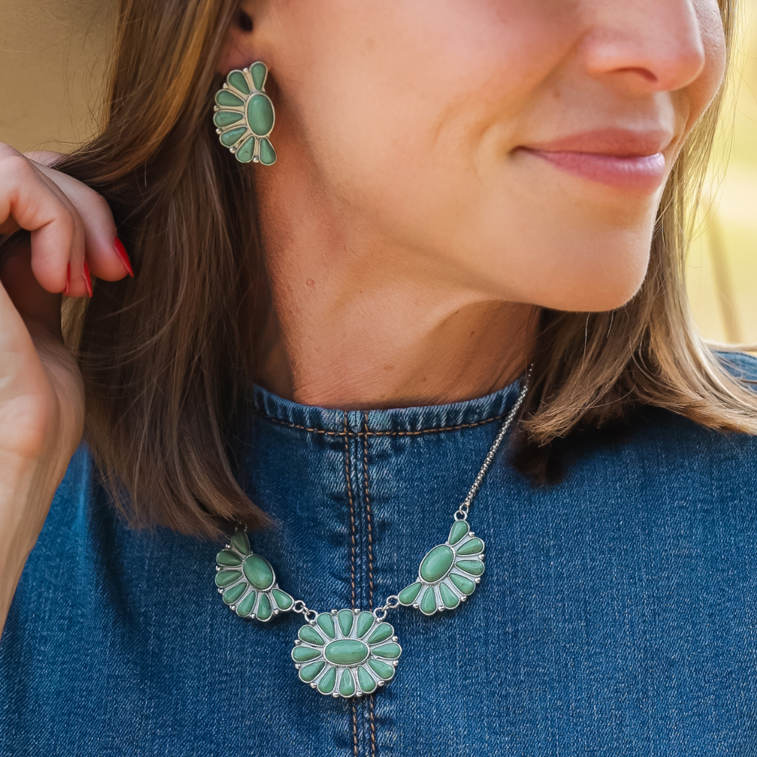 Woman wearing a denim top and The Fern Stud Earrings in green turquoise, smiling gently while touching her ear, with shoulder-length brown hair—her jewelry adds a touch of Western charm to her look.