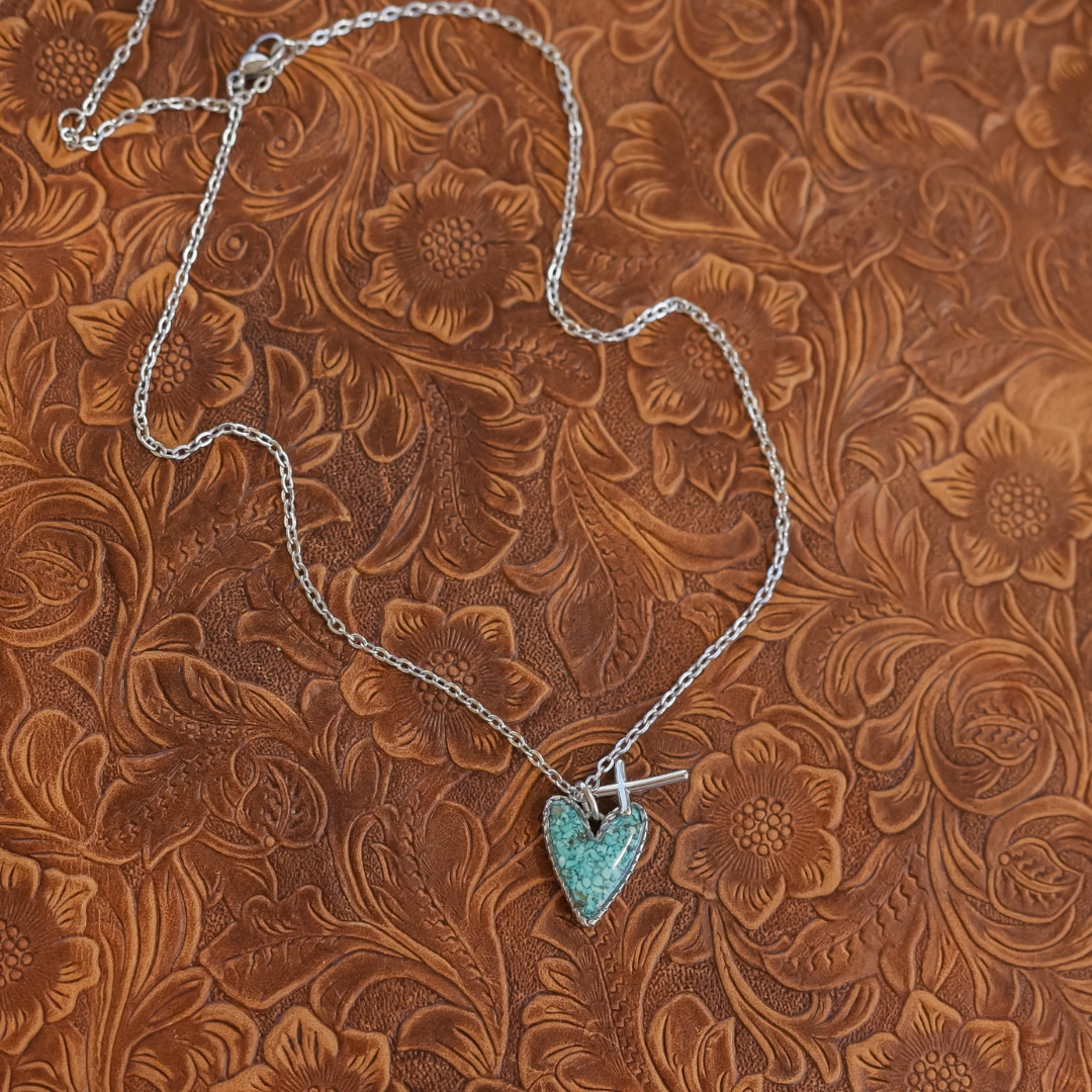 The Grace necklace featuring a heart-shaped turquoise pendant layered behind a small silver cross charm.