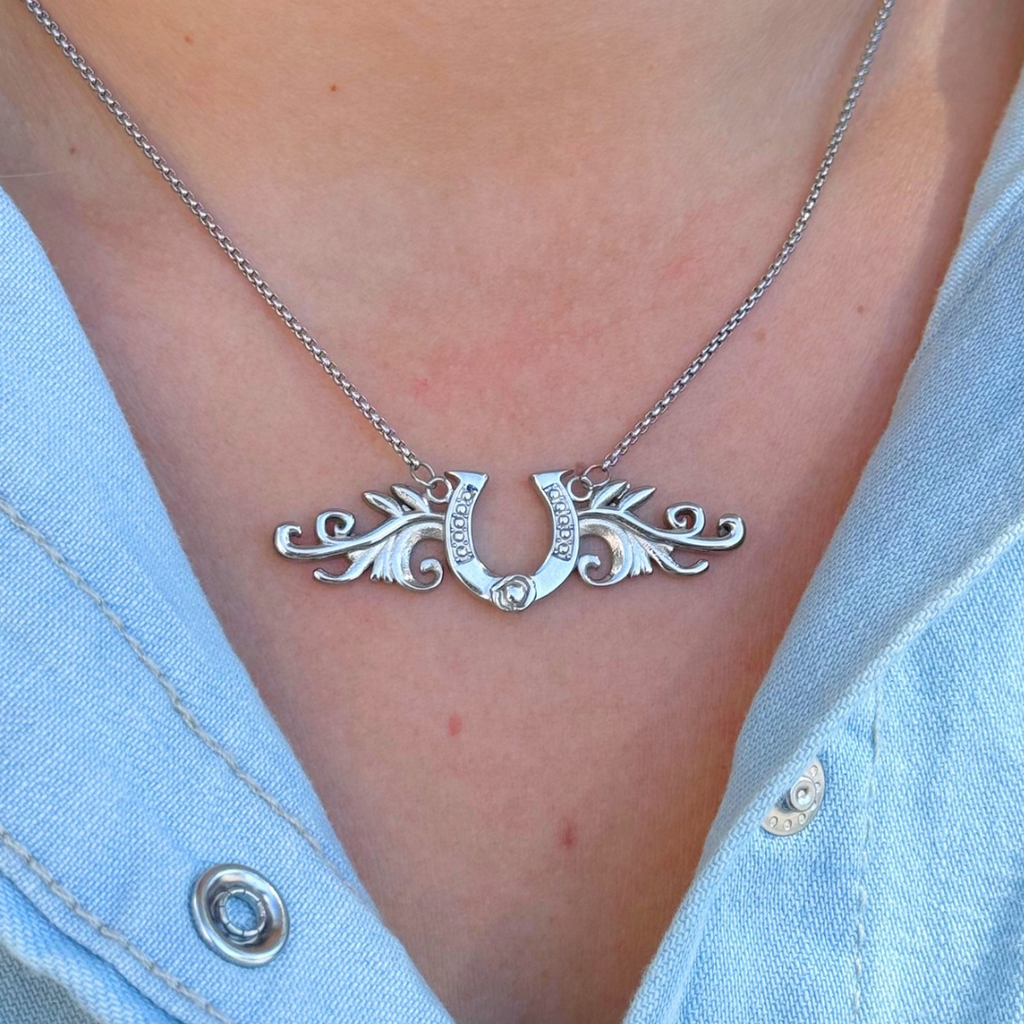 The Gretel silver horseshoe necklace features a charm framed by ornate filigree wings, worn as a lucky pendant.