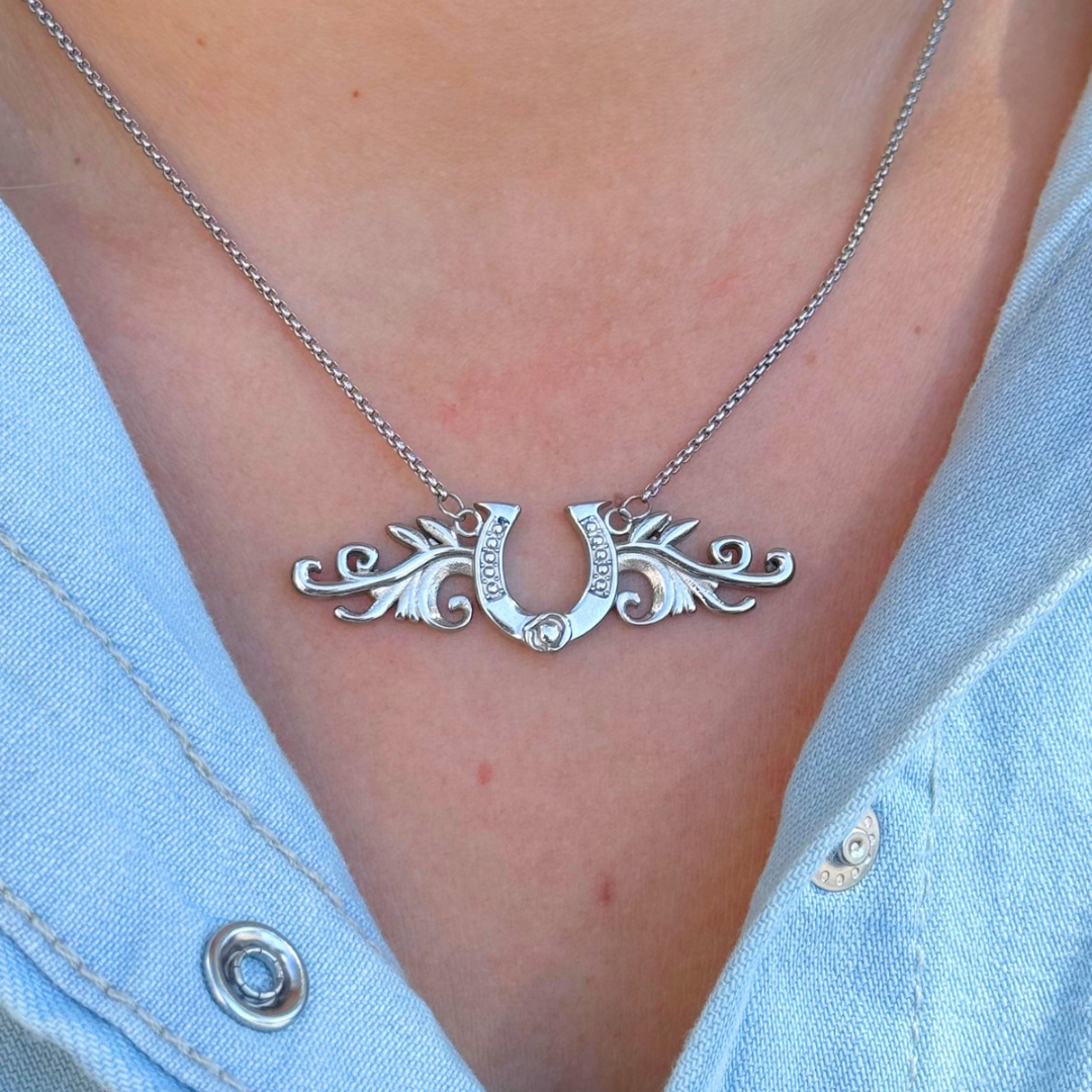 The Gretel silver horseshoe necklace features a charm framed by ornate filigree wings, worn as a lucky pendant.