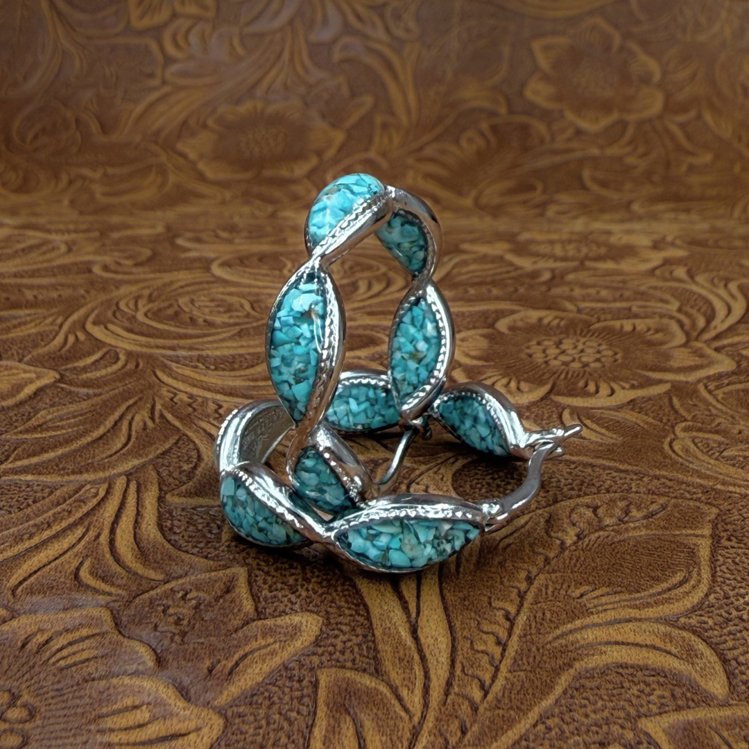 The Janell Hoops, featuring silver hoops with turquoise stone inlays, rest on embossed brown leather with a floral pattern, capturing the essence of classic Western style jewelry.