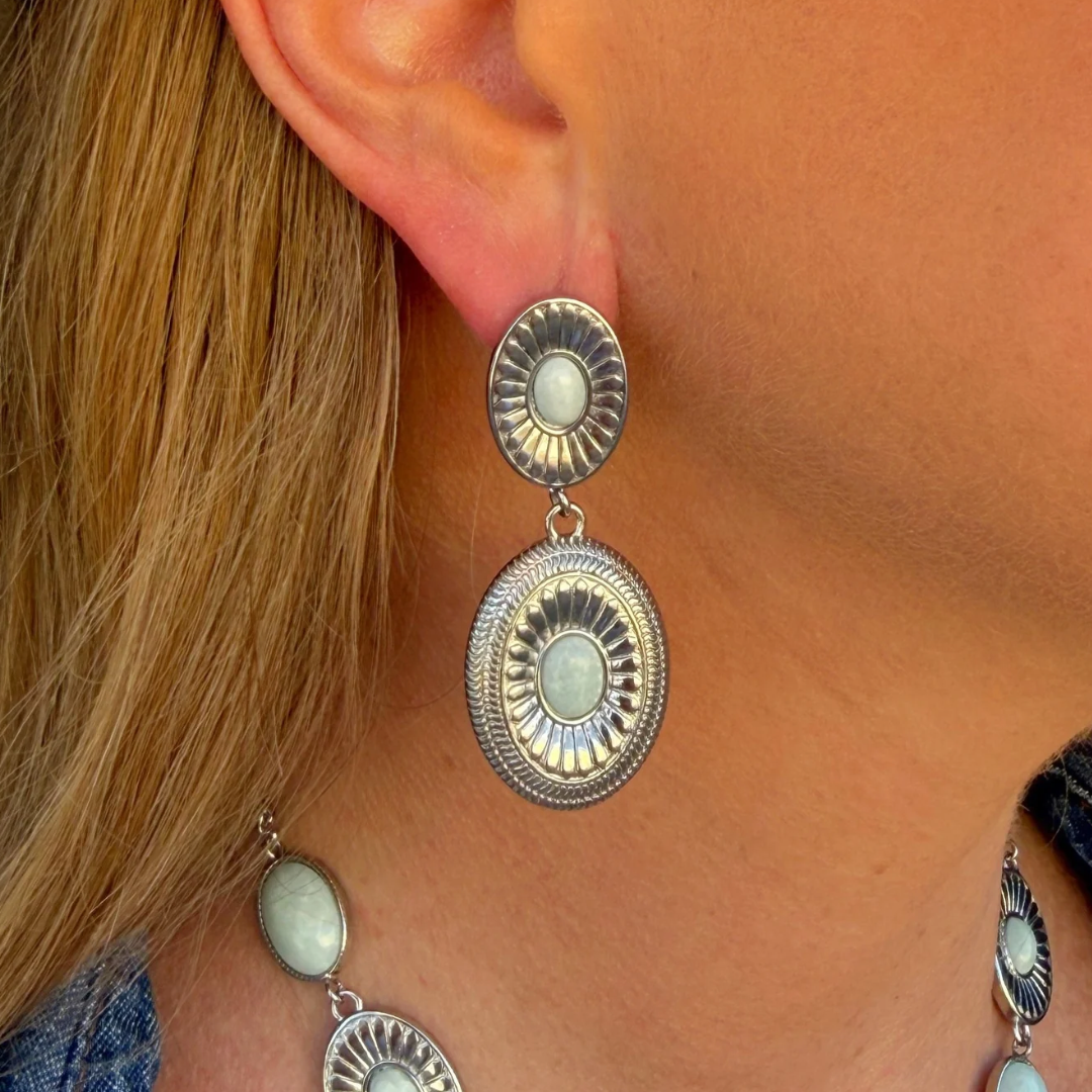 The Kathryn Drop Earrings are silver Western-style drops featuring two oval, sunburst-patterned charms set with pale green cabochon stones.