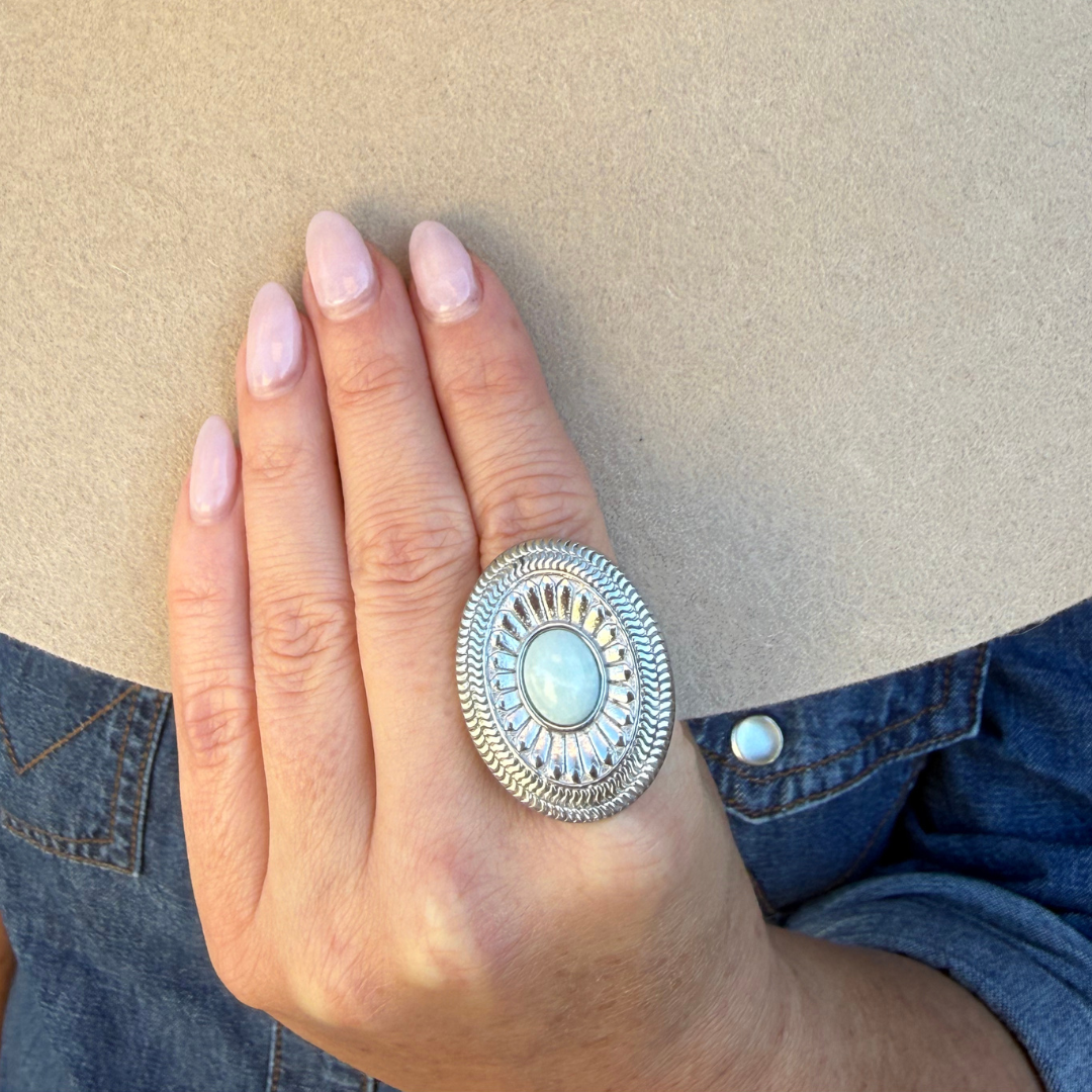 The Kathryn Ring is a silver-toned oval ring featuring an etched sunburst design and a central, smooth light blue stone in a Western style, worn on a finger.