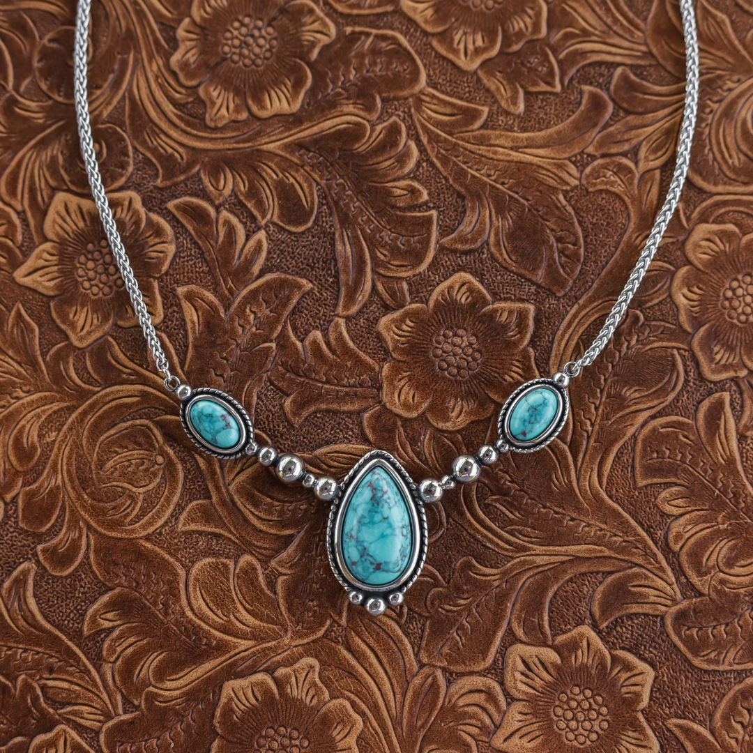 The Kay is a silver Western necklace featuring a large, central teardrop-shaped turquoise stone flanked by two smaller oval turquoise stones on a silver chain.