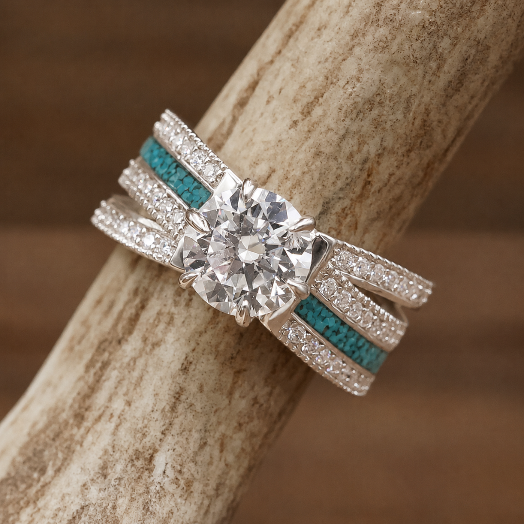 The Lux Grand Chelly, a silver western-style ring adorned with a large round clear gemstone, turquoise inlays, and small clear stones on the band, is displayed on a textured beige surface.