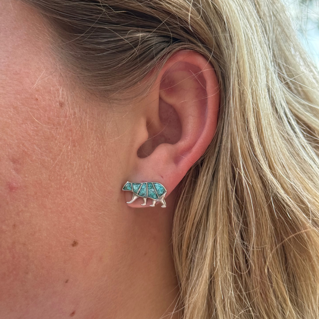 A close-up of a light-skinned, blonde-haired person’s ear wearing the Mama Bear Stud Earrings, featuring turquoise and silver bear silhouettes.