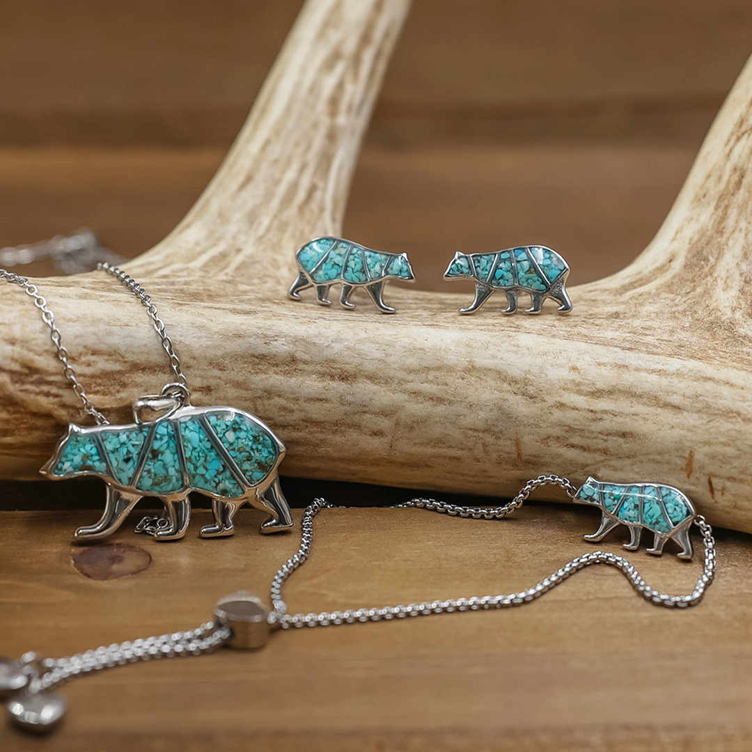 Sterling silver Mama Bear Stud Earrings with turquoise inlay, elegantly shaped like bears, displayed alongside a matching necklace on a wooden surface with an antler in the background—an ideal choice for meaningful motherhood jewelry that beautifully balances sentiment and style.