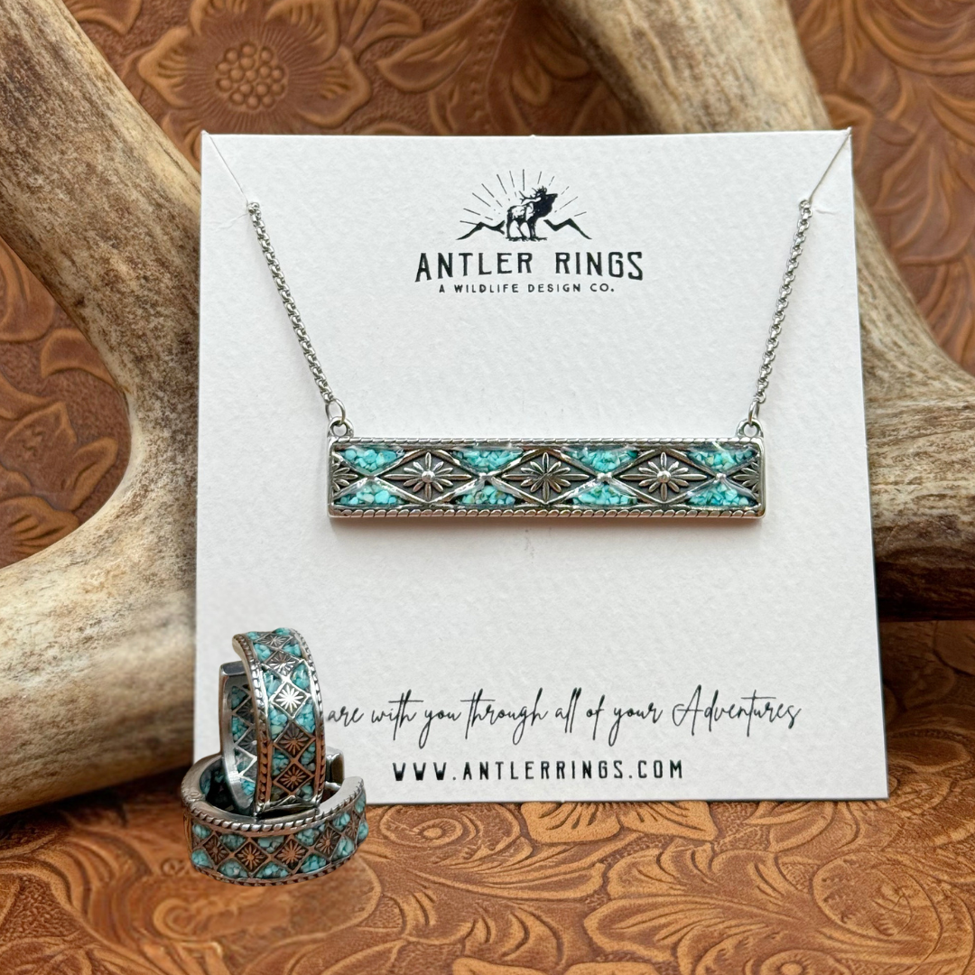 Rectangular turquoise and silver necklace displayed with matching rings on an Antler Rings card. The card features a deer logo and website, with antlers and a tooled leather background, capturing the authentic charm of Western jewelry. For a complete Southwestern-inspired look, consider pairing this set with The Meggan Hoops.