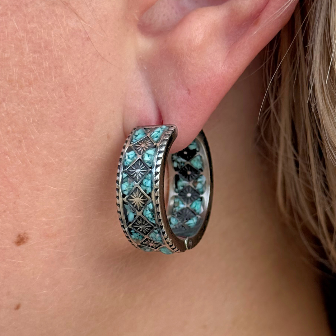 A close-up of an ear adorned with The Meggan Hoops, silver hoop earrings featuring turquoise and black geometric patterns with intricate star-shaped designs. These stylish earrings highlight the artistry of Western jewelry, making The Meggan Hoops a stunning example of turquoise hoop earrings.