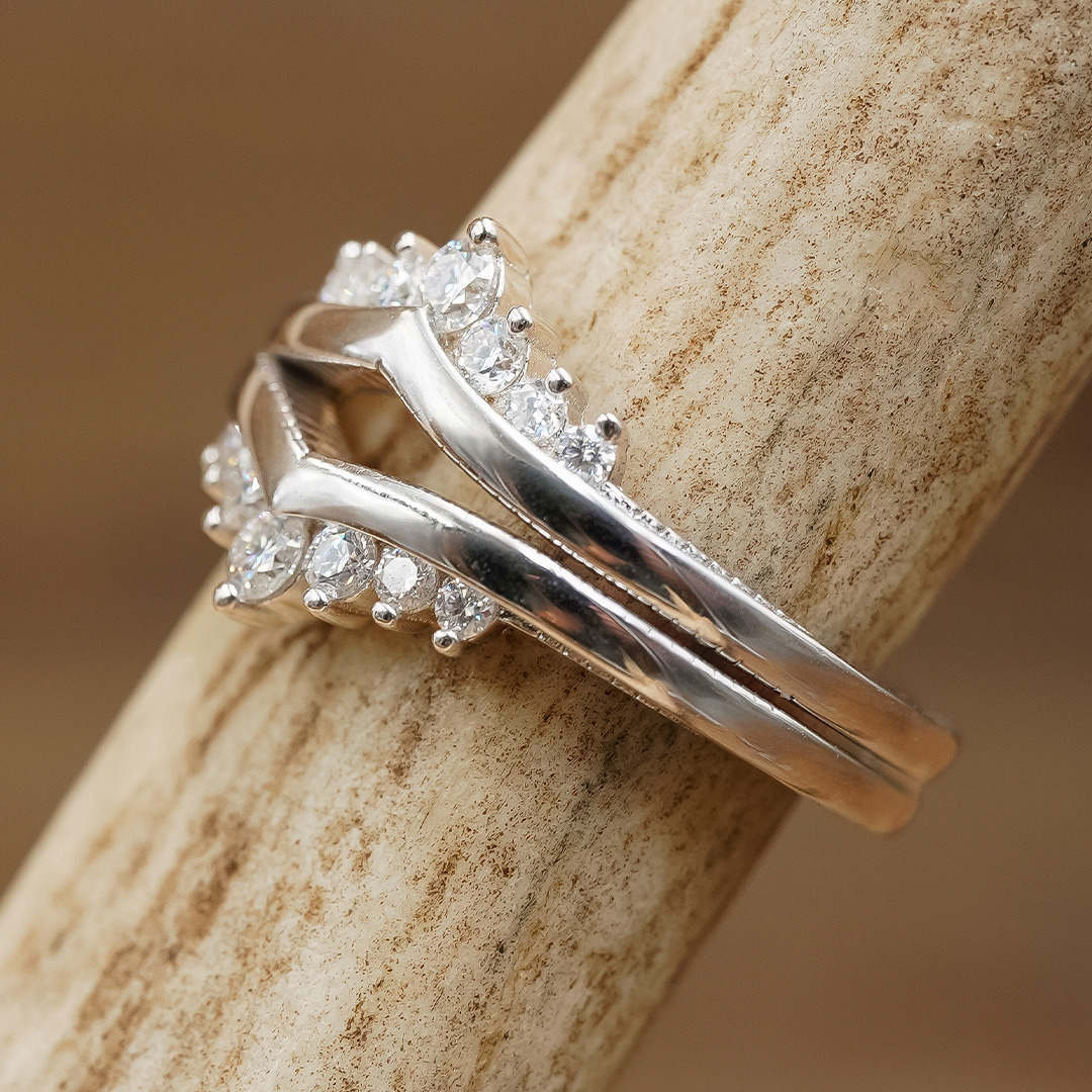 The Moissanite Wishbone Stacker Set, crafted from sterling silver and featuring small, clear moissanite gemstones in a cluster design, is photographed resting on a textured beige surface.