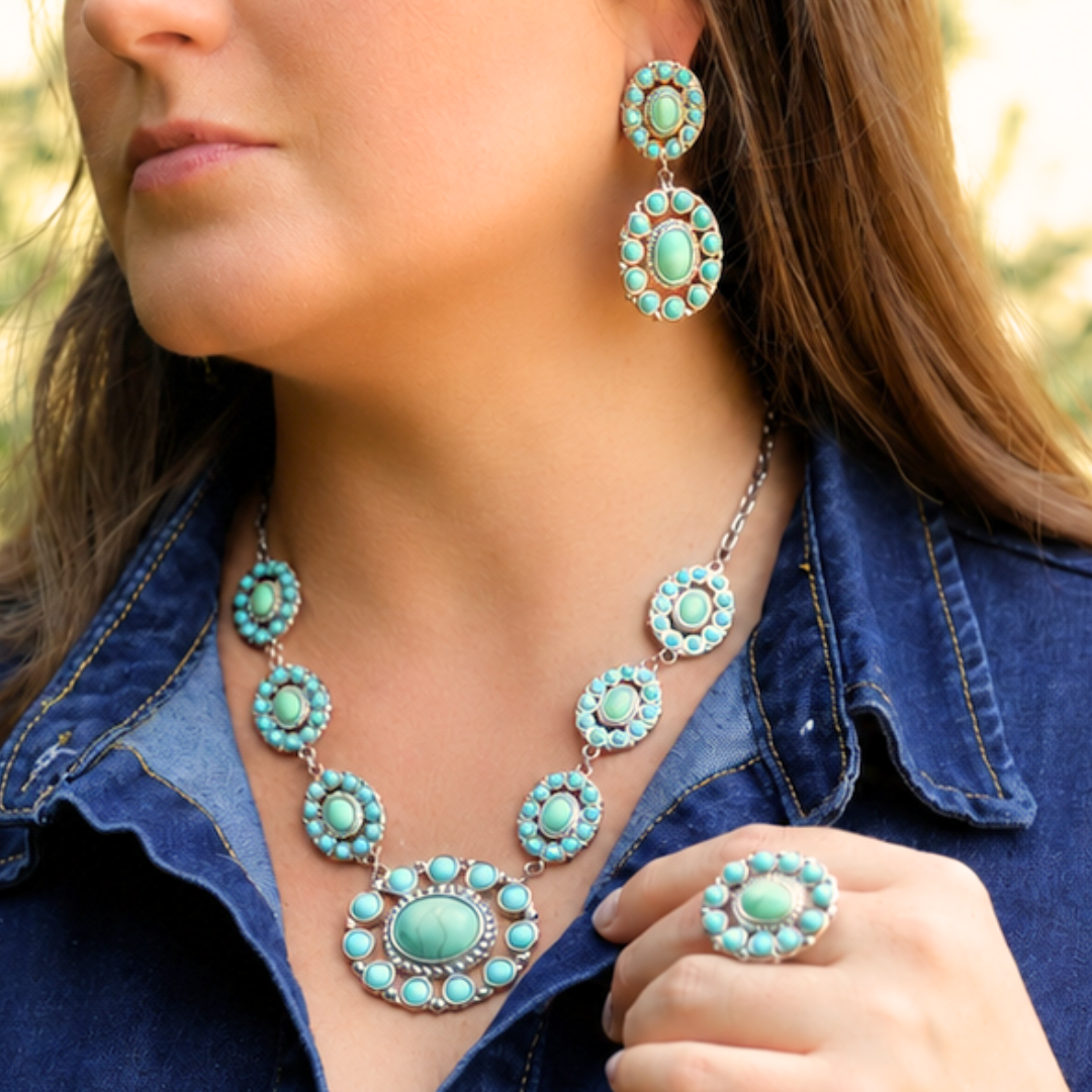 Woman wearing a denim shirt, turquoise statement necklace, matching earrings, and The Nellie Ring—a bold Western statement ring—posing outdoors.