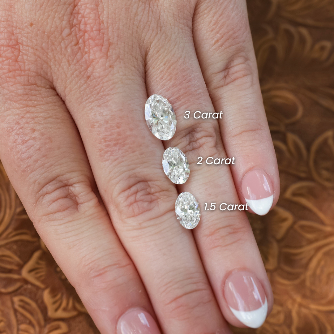A hand with French manicured nails displays an IGI Certified 1.5 ct. oval cut lab-grown diamond with VS1 clarity, placed on the ring finger against a brown patterned background.