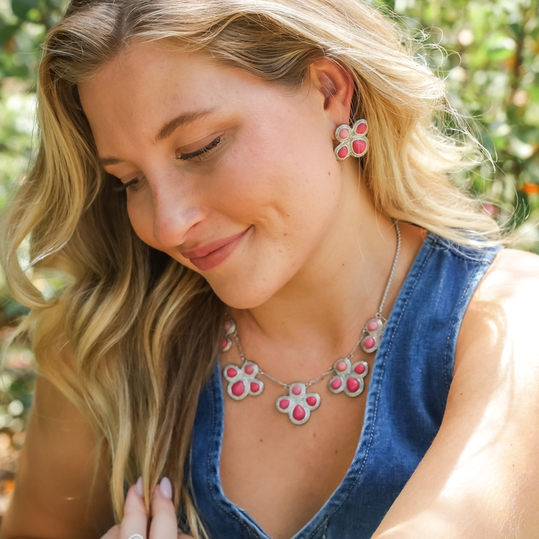 A woman wears The Prairie Rose, a Western-style silver necklace and matching earring set featuring pink, four-petaled flower shapes.