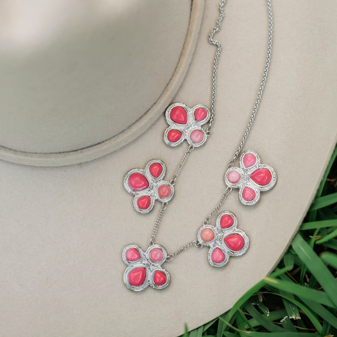 The Prairie Rose silver chain necklace featuring four flower-shaped charms with pink teardrop-shaped stones, lying on a beige hat as a Western style statement piece.