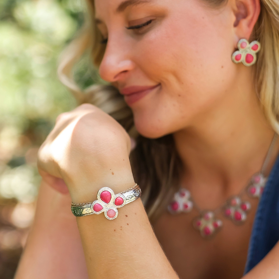 A smiling woman wears Western jewelry including a matching Prairie Rose Cuff, necklace, and earrings featuring silver settings and pink stones.
