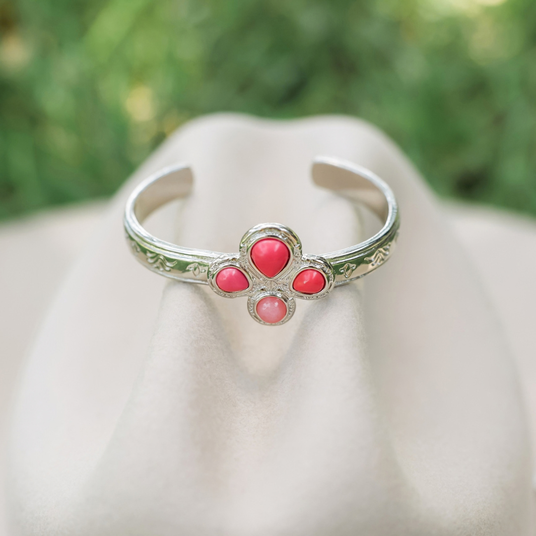 The Prairie Rose Cuff is a silver bracelet featuring an engraved band and a four-stone cluster of pink, teardrop-shaped cabochons.