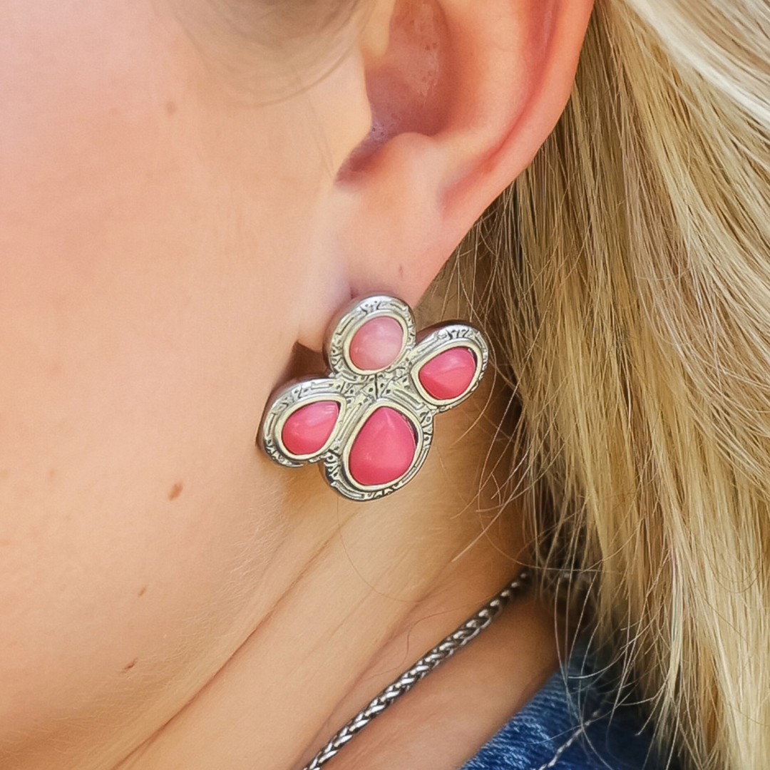 A person wearing silver-toned Prairie Rose Studs, each shaped like a four-petaled flower with a smooth pink stone.
